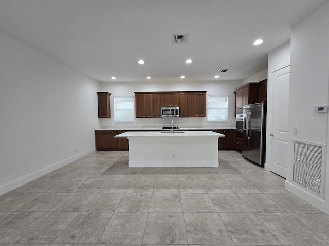 kitchen with appliances with stainless steel finishes, light countertops, visible vents, and a kitchen island with sink