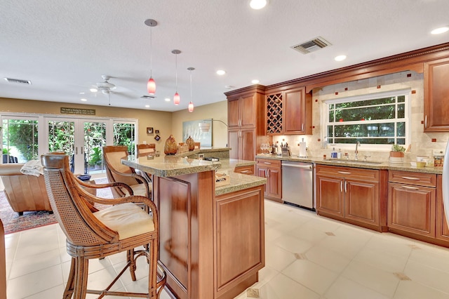 kitchen featuring light stone counters, stainless steel dishwasher, sink, decorative light fixtures, and a kitchen island