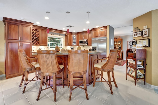 bar featuring pendant lighting, stainless steel appliances, light tile patterned floors, and dark stone countertops