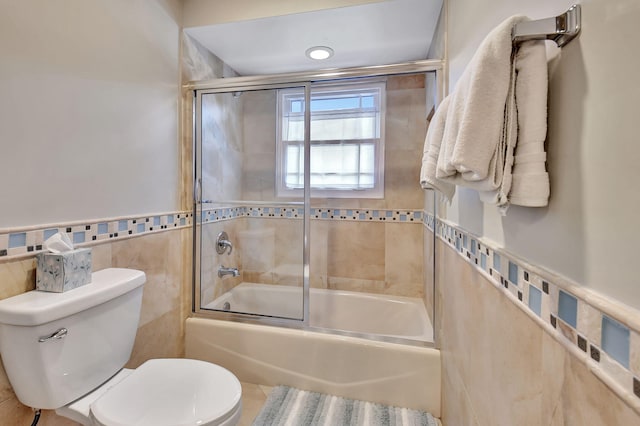 bathroom with enclosed tub / shower combo, tile walls, and toilet