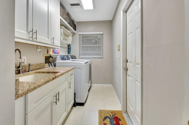 clothes washing area with cabinets, light tile patterned flooring, washing machine and dryer, and sink