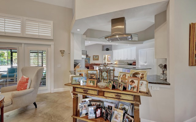 interior space featuring island range hood, sink, light tile patterned floors, white cabinets, and a towering ceiling