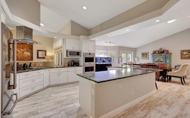 kitchen featuring stainless steel appliances, wall chimney exhaust hood, dark stone counters, and white cabinets