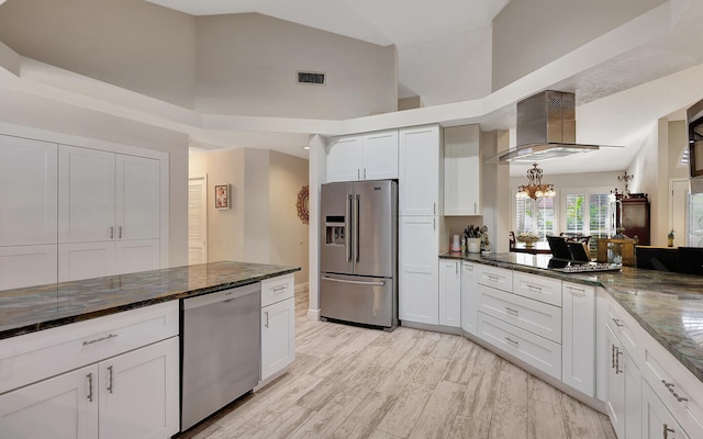 kitchen featuring wall chimney exhaust hood, stainless steel appliances, dark stone counters, light wood-type flooring, and white cabinetry