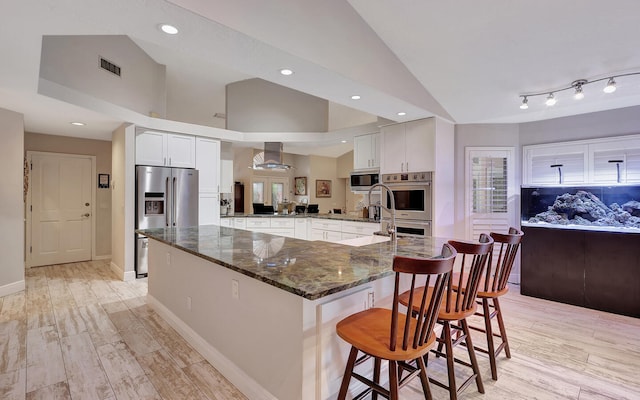 kitchen with light hardwood / wood-style flooring, vaulted ceiling, white cabinets, dark stone countertops, and a breakfast bar