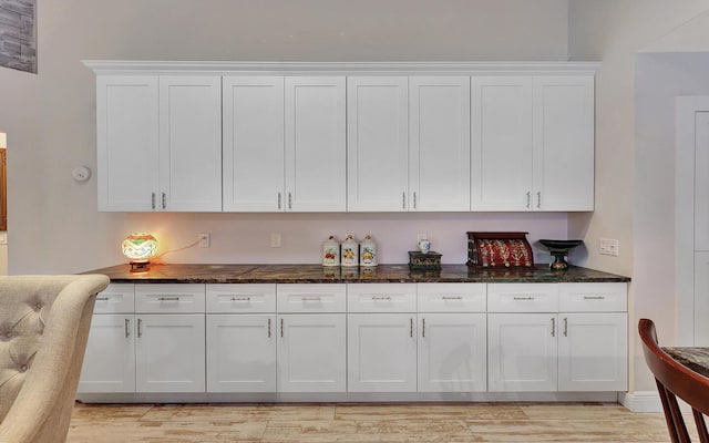 bar with white cabinets, light hardwood / wood-style flooring, and dark stone counters