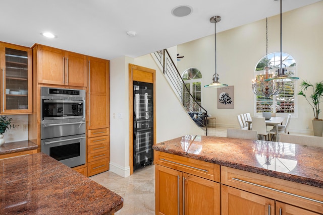 kitchen featuring wine cooler, dark stone countertops, an inviting chandelier, decorative light fixtures, and stainless steel double oven