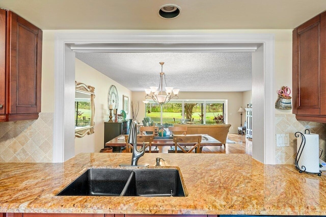 kitchen with an inviting chandelier, decorative backsplash, sink, and light stone counters