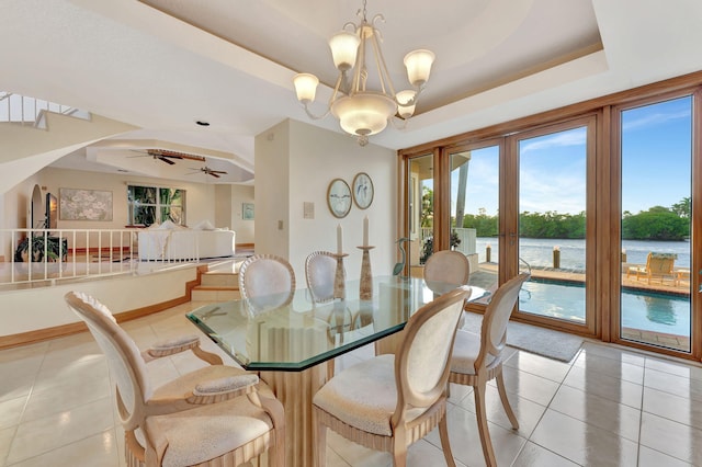 tiled dining room featuring french doors, ceiling fan with notable chandelier, a water view, and a raised ceiling