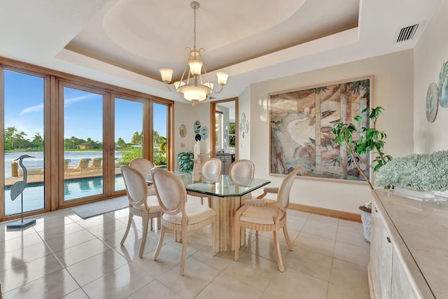 dining area with light tile patterned floors, a water view, a raised ceiling, and a notable chandelier