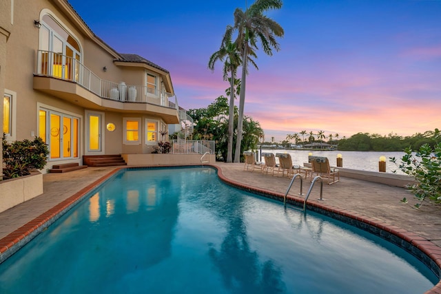 pool at dusk with a water view and a patio area