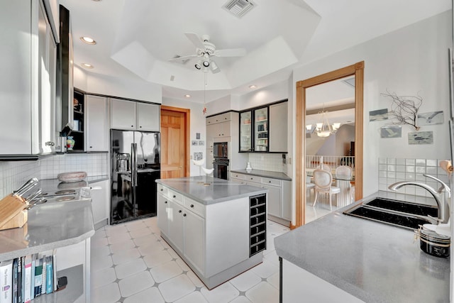 kitchen featuring tasteful backsplash, a raised ceiling, sink, black appliances, and a center island