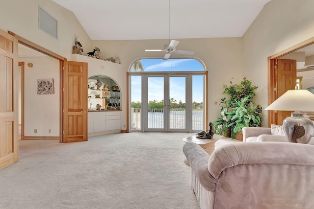 carpeted living room with ceiling fan, a water view, high vaulted ceiling, and built in shelves