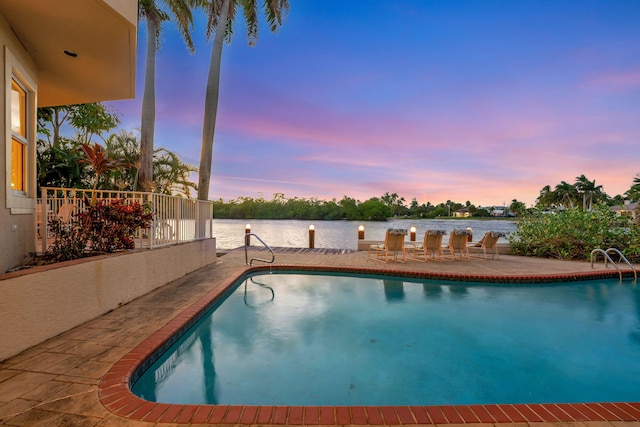 pool at dusk featuring a patio area and a water view