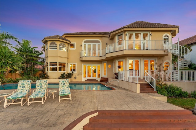 back house at dusk featuring a balcony and a patio