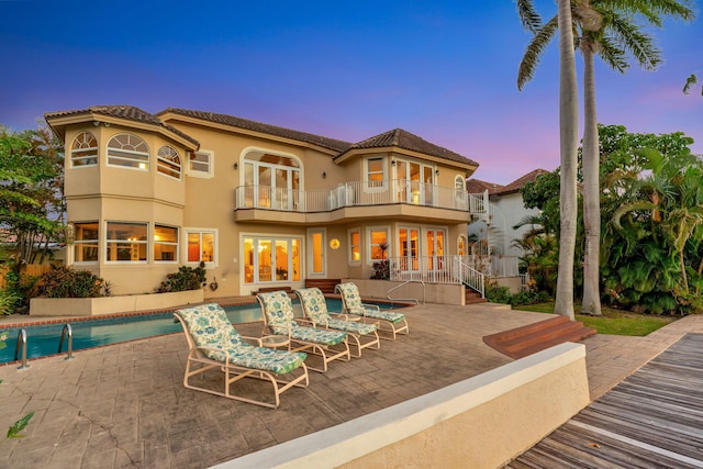 back house at dusk with a balcony and a patio area