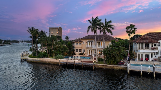 back house at dusk with a water view, a balcony, and a patio