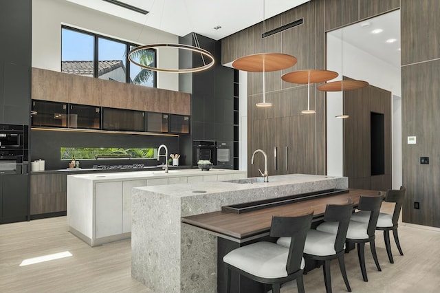 kitchen featuring an island with sink, a high ceiling, dark brown cabinets, a breakfast bar area, and decorative backsplash