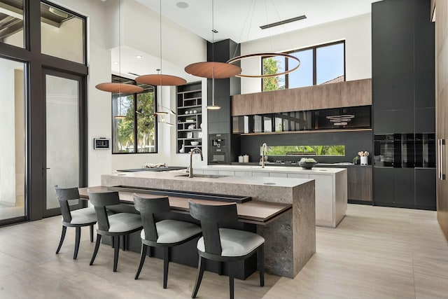 kitchen with sink, a center island with sink, a towering ceiling, and a wealth of natural light