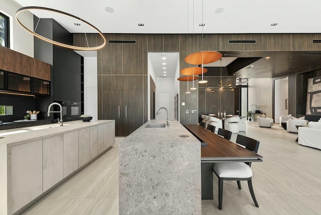 kitchen with a towering ceiling, a large island with sink, sink, light stone counters, and pendant lighting