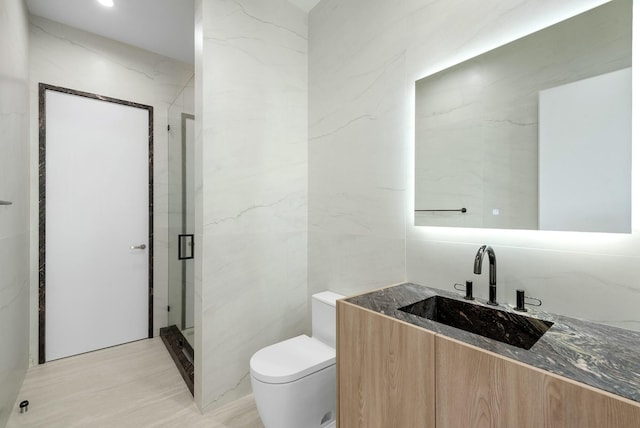 bathroom featuring toilet, tile walls, vanity, and a shower with door