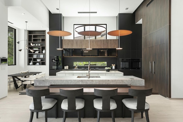 kitchen featuring an island with sink, dark brown cabinetry, a high ceiling, and sink