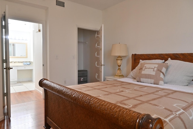 bedroom featuring a spacious closet, light hardwood / wood-style flooring, ensuite bath, and a closet