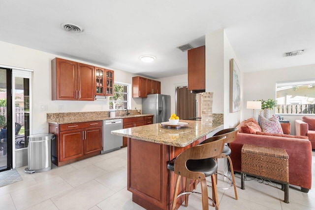 kitchen featuring stainless steel appliances, light stone counters, kitchen peninsula, a breakfast bar area, and light tile patterned floors