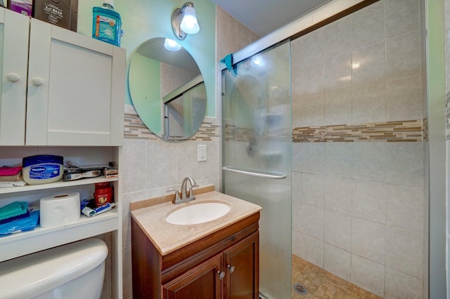 bathroom with toilet, decorative backsplash, vanity, a shower with shower door, and tile walls