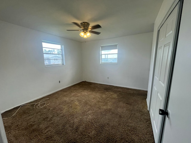 empty room with a healthy amount of sunlight, ceiling fan, and dark carpet