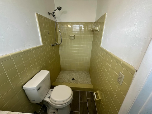 bathroom with toilet, a tile shower, and tile walls