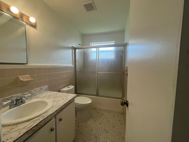 full bathroom featuring tile patterned flooring, enclosed tub / shower combo, vanity, toilet, and tile walls