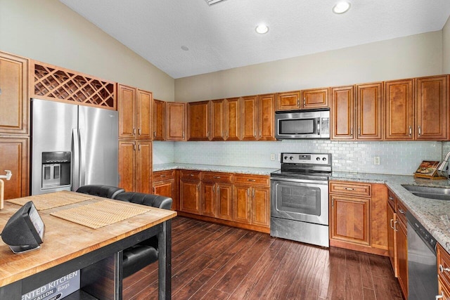 kitchen featuring light stone counters, appliances with stainless steel finishes, backsplash, lofted ceiling, and dark wood-type flooring