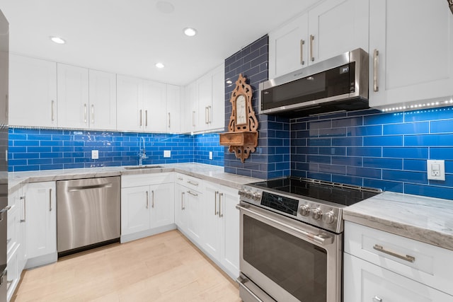 kitchen featuring tasteful backsplash, light stone counters, light wood-type flooring, appliances with stainless steel finishes, and white cabinets