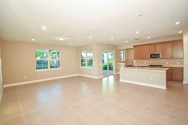 kitchen with decorative backsplash, sink, a center island with sink, and light tile patterned flooring