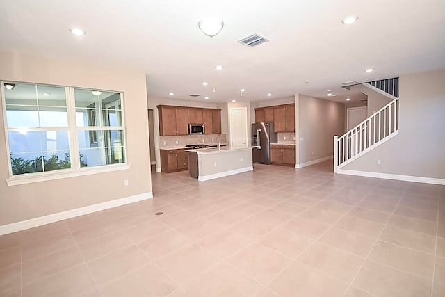 kitchen featuring backsplash, an island with sink, light tile patterned floors, and appliances with stainless steel finishes