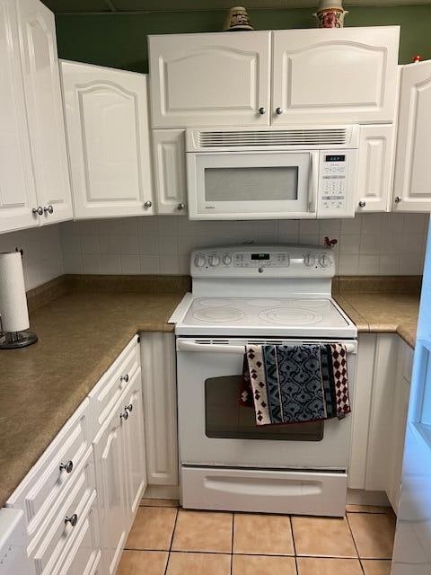 kitchen featuring white appliances, white cabinetry, light tile patterned flooring, and decorative backsplash