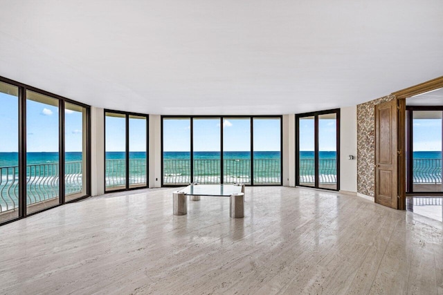 spare room with a water view, light hardwood / wood-style floors, expansive windows, and a beach view