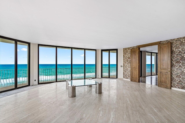 spare room featuring a water view, light wood-type flooring, and floor to ceiling windows