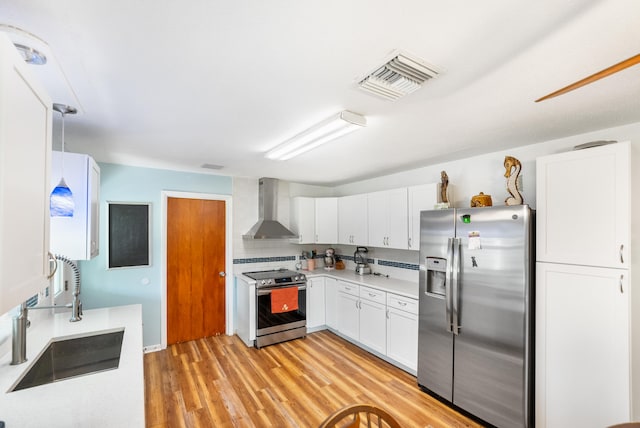 kitchen with appliances with stainless steel finishes, sink, white cabinetry, wall chimney exhaust hood, and pendant lighting