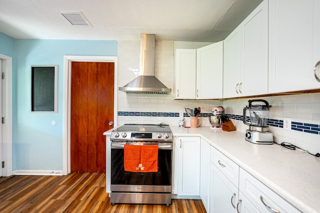 kitchen featuring wall chimney range hood, stainless steel electric stove, white cabinetry, decorative backsplash, and dark hardwood / wood-style floors