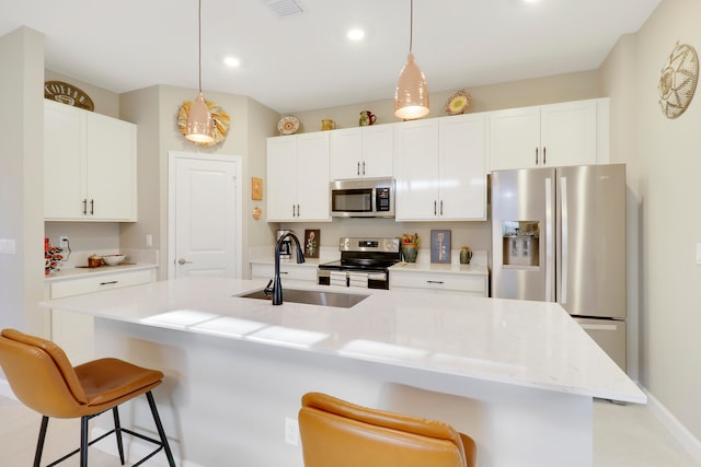 kitchen with appliances with stainless steel finishes, hanging light fixtures, white cabinets, and an island with sink