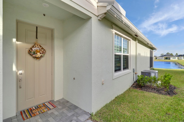 entrance to property with a water view, a lawn, and cooling unit