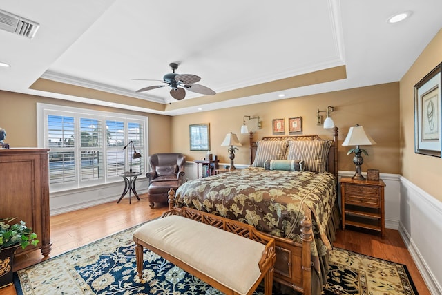 bedroom with hardwood / wood-style flooring, ceiling fan, crown molding, and a tray ceiling