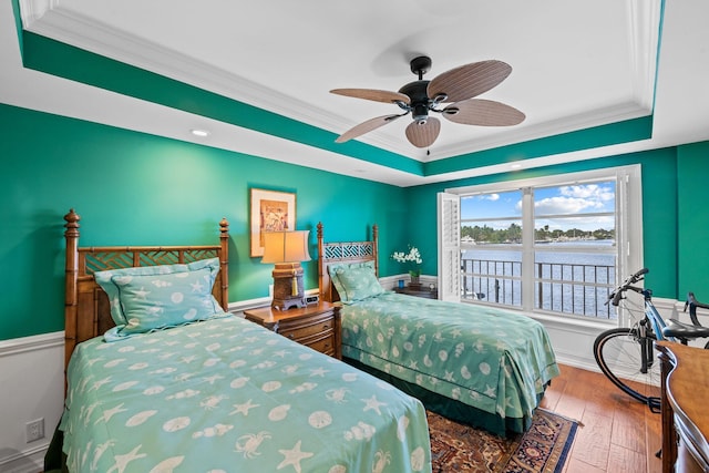 bedroom with wood-type flooring, crown molding, a water view, a tray ceiling, and ceiling fan