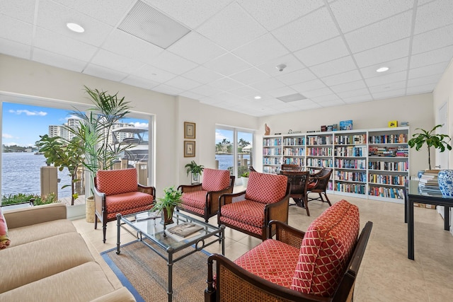 living room featuring a paneled ceiling, a water view, and light tile patterned floors