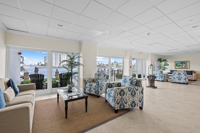 living room with a water view, a drop ceiling, tile patterned flooring, and a healthy amount of sunlight