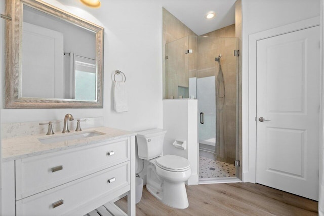 bathroom with toilet, vanity, wood-type flooring, and a shower with door