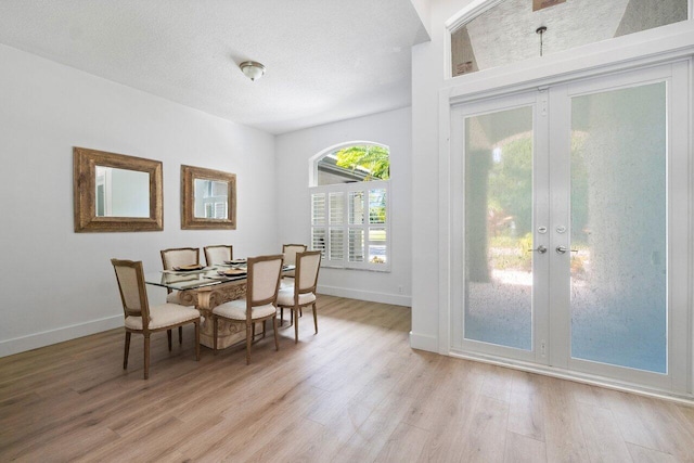 dining area with french doors, light wood-type flooring, and a textured ceiling