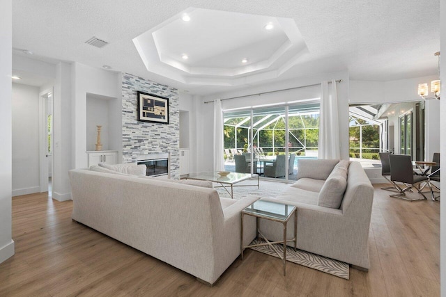 living room featuring a fireplace, light hardwood / wood-style floors, a textured ceiling, and a raised ceiling